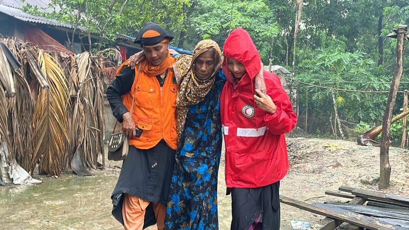 A Bangladesh Red Crescent volunteer helps a lady away from her flooded home following Cyclone Remal. The response was part funded through an IFRC-DREF allocation Photo: BRCS